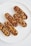 Five elongated pastries filled with a variety of nuts and seeds, drenched in a glossy caramelized coating, are arranged on a clean, white plate. The nuts and seeds include almonds, hazelnuts, and pistachios, contributing to a rich texture and appearance.