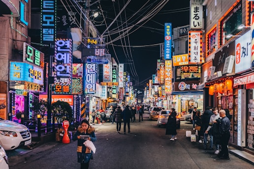 A vibrant night scene of a bustling street in Busan filled with neon lights and lively crowds.