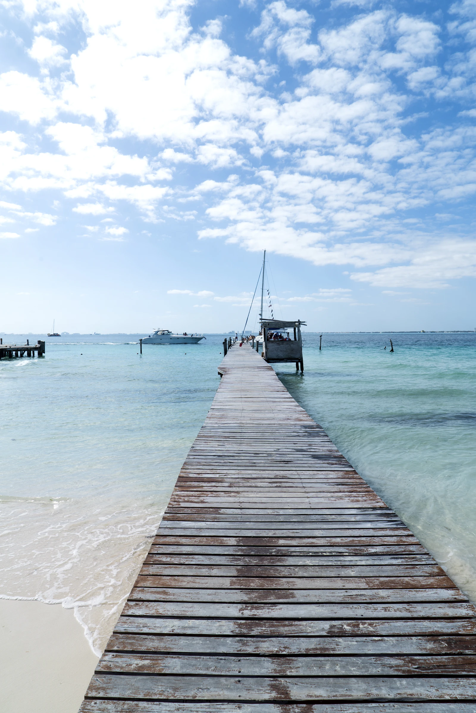 Wooden pier reaching into turquoise Caribbean shallows with sailboats moored off Isla Mujeres near Cancún