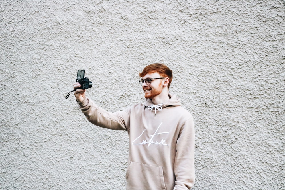 man taking selfie in front of gray wall