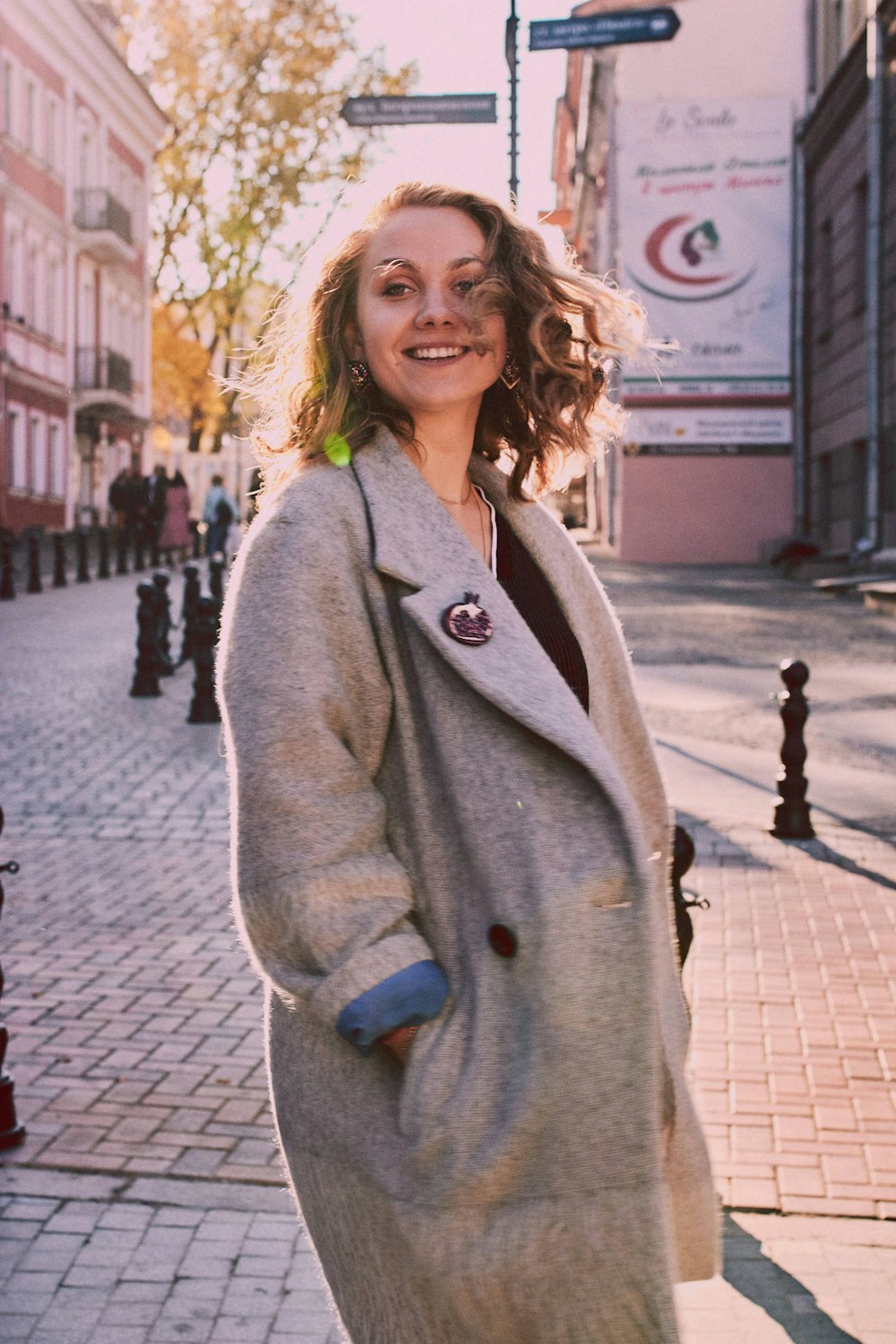 woman with hands in her overcoat smiling and standing near buildings during day
