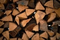 A close-up view of a neatly stacked pile of chopped firewood. The logs are cut into triangular and polygonal shapes, showing various textures and grain patterns. Some have darkened edges or markings, indicating aging or exposure to elements.