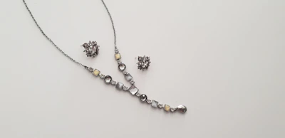 Elegant necklace and earrings set displayed on a minimalist ivory stand with soft shadows.