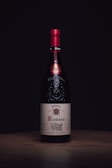 A wine bottle with a red cap and an elegant label displaying the name 'Rasteau'. The bottle stands on a wooden surface against a dark background, highlighting its sophisticated design.