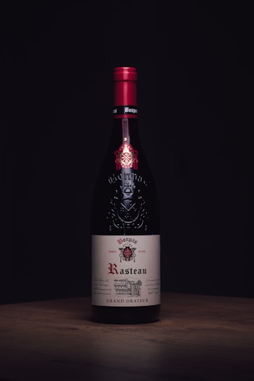 A close-up of a deep red wine bottle with elegant label against a rustic wooden background.