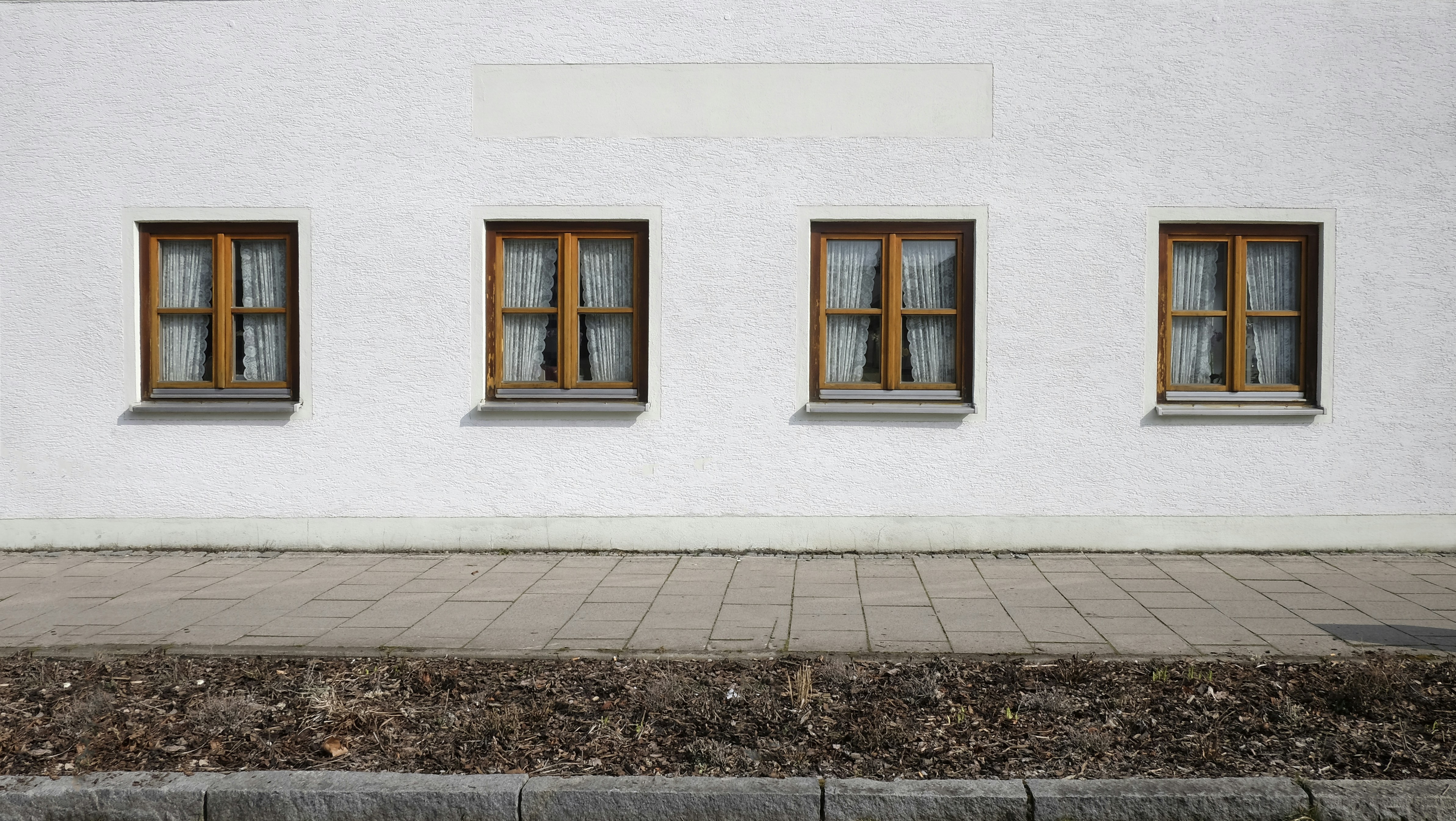 Four, square, old wooden windows on a white building's wall.
