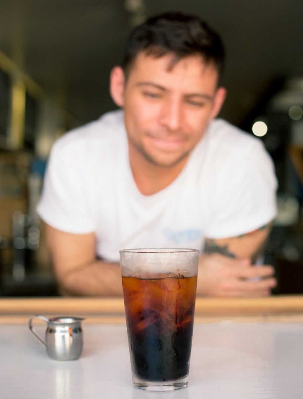 smiling man leaning on beige table looking on cup with liquid inside