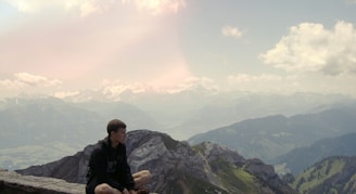 A person sitting on a mountain peak, gazing at the vast horizon with a calm smile.