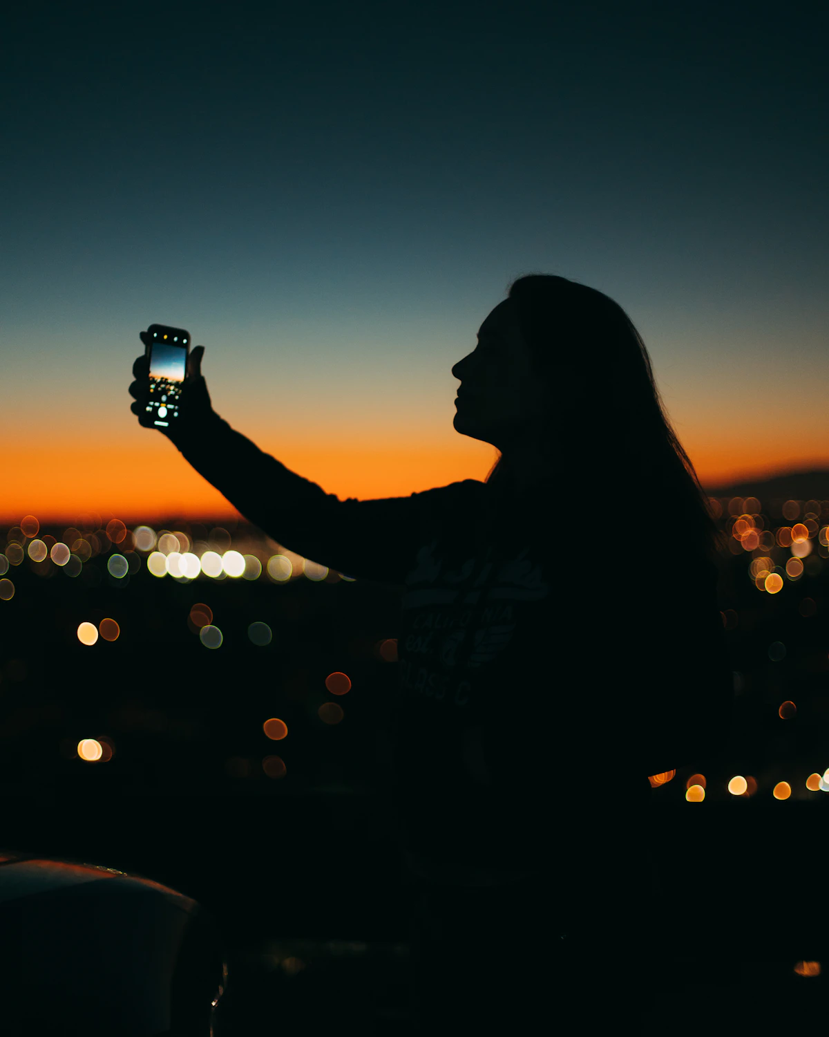 Siluet seorang perempuan memegang ponsel dalam gelap