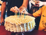 Hands decorating a multi-layered cake with colorful fondant flowers.