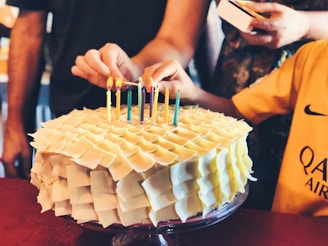 Hands decorating a multi-layered cake with colorful fondant flowers.