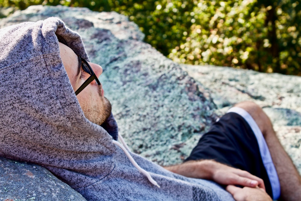 man wearing hoodie leaning on stone