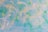 The image features a brick wall painted with blue, green, and hints of yellow. The colors blend together in a swirl-like pattern, giving the wall a vibrant, artistic look.