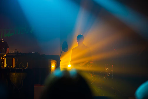 Tomy Jabana illuminated by red and orange stage lights, embodying the fire of his groove.