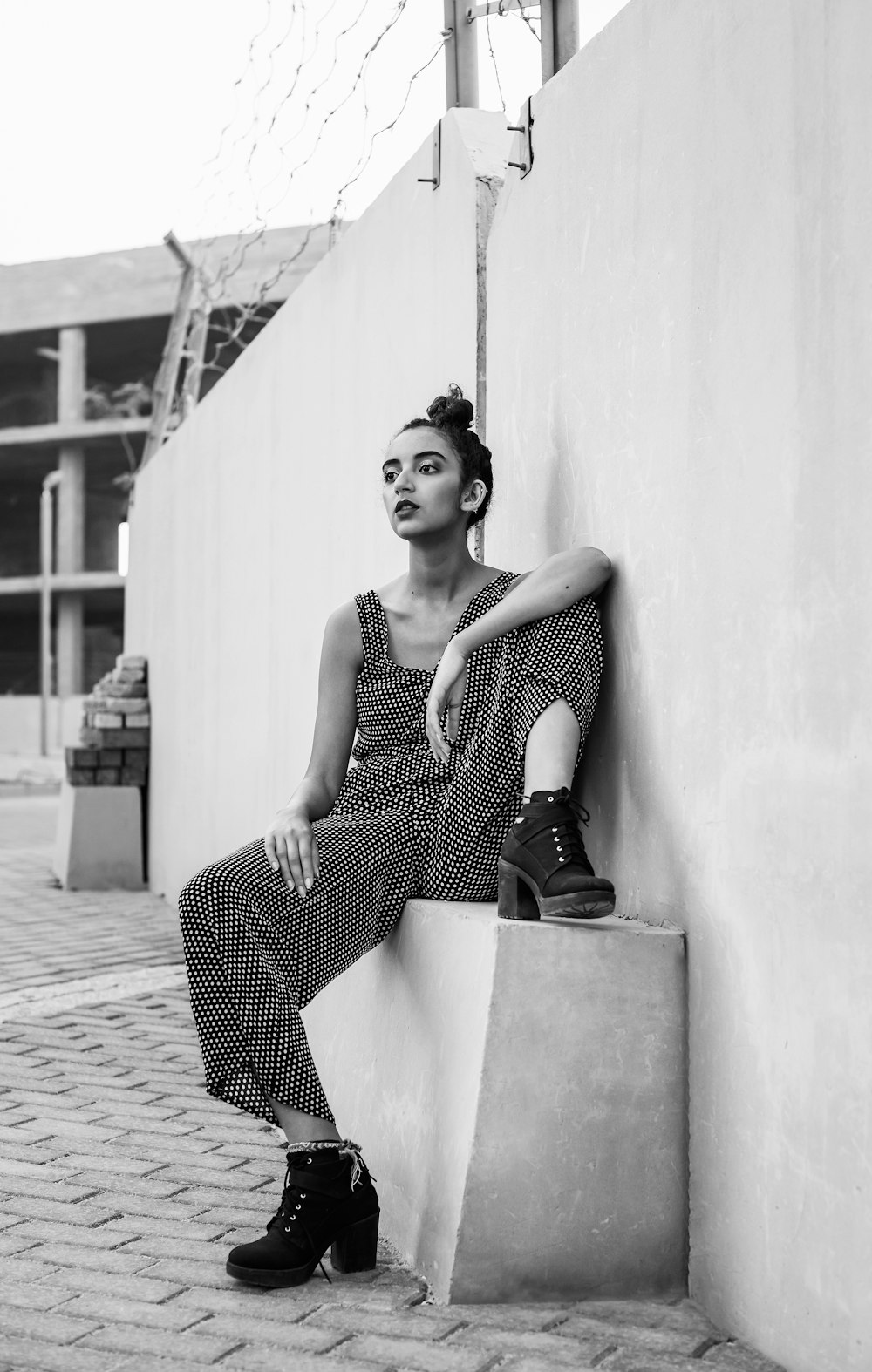 greyscale photo of woman wearing black romper while sitting near wall