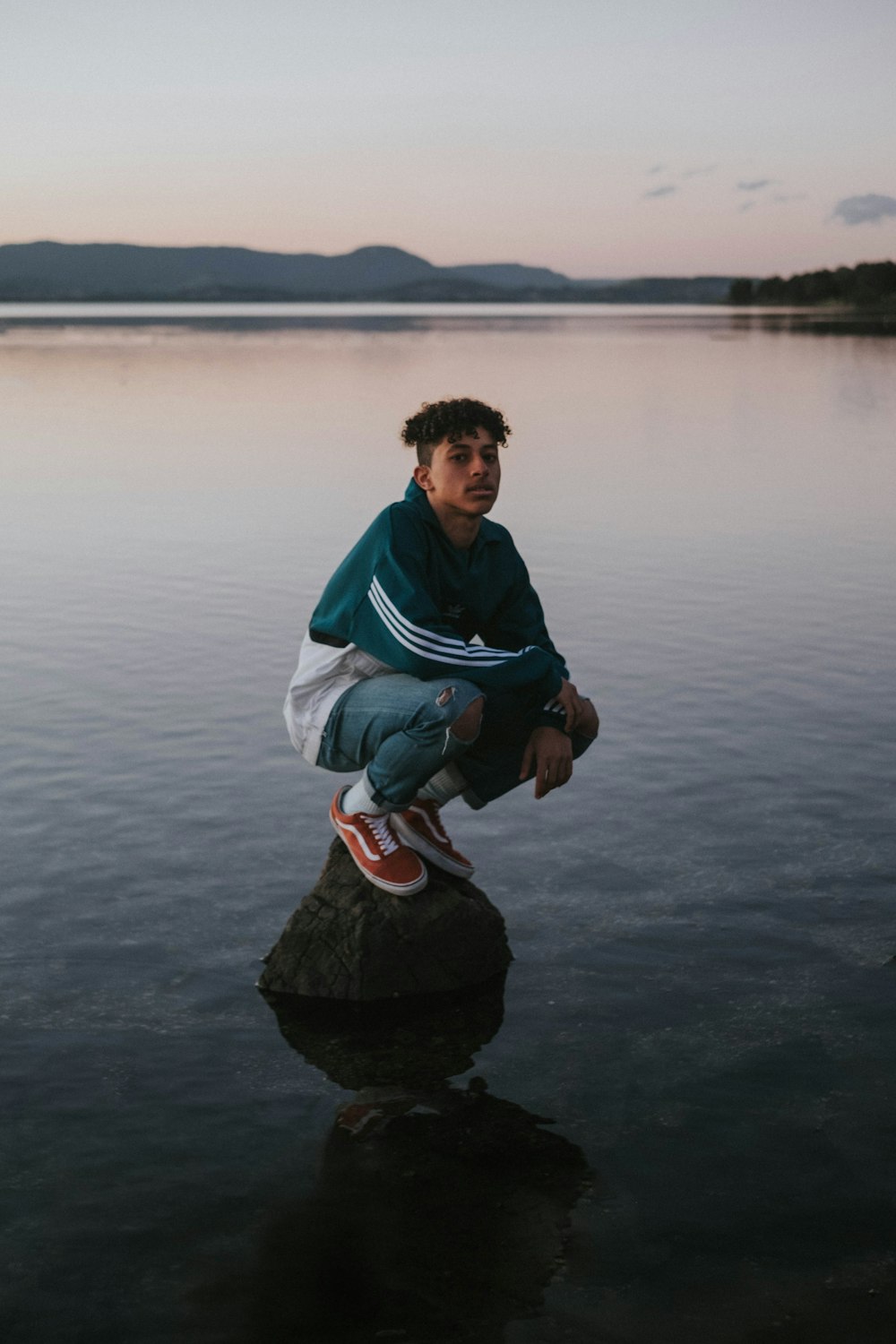 man sitting on the rock surrounded by body of waters