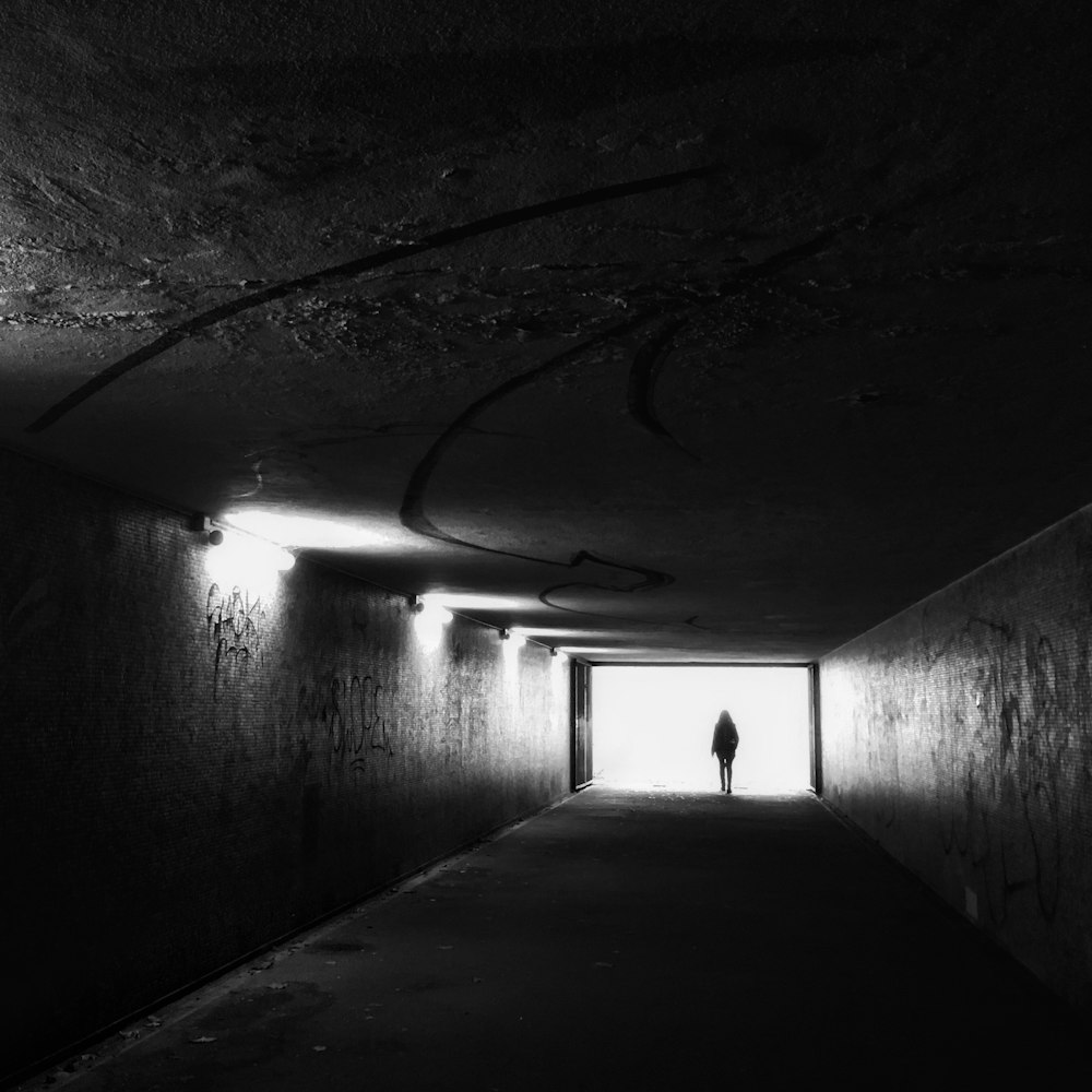 grayscale photography of man standing in tunnel