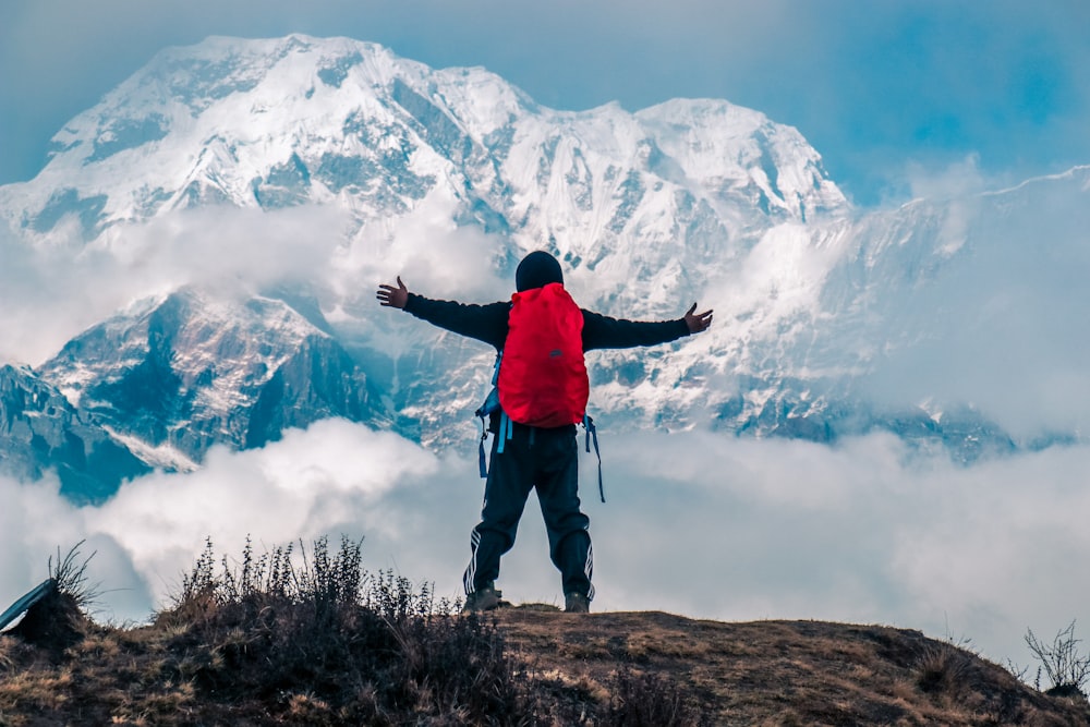 hombre levantando ambas manos en el acantilado de la montaña con la vista de la montaña cubierta de nieve