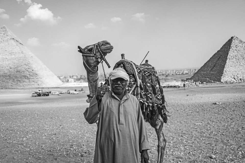 Homem com camelo em pé no deserto perto de pirâmides