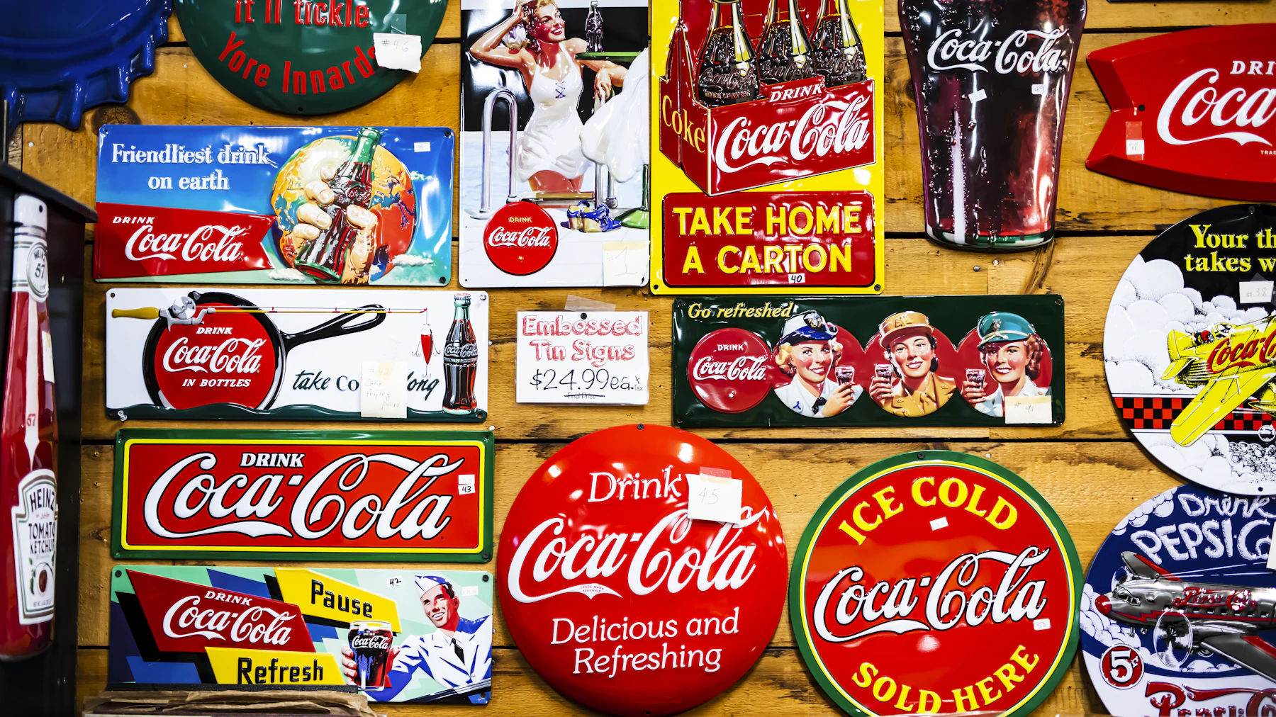 A wooden wall covered in round, rectangular and bottle-shaped Coca-Cola tin signs
