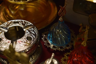 A collection of intricately designed metal and glass objects featuring elaborate patterns and vibrant colors. The metal object has ornate engravings, while the glass objects have a teardrop shape and are placed on decorative bases.
