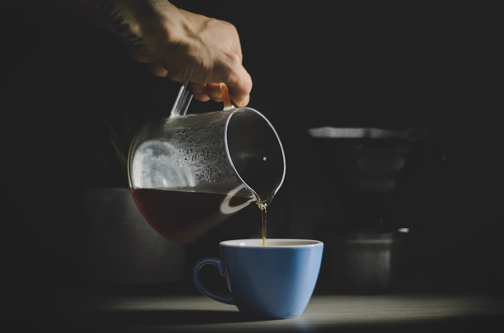 person pouring brown liquid on teacup