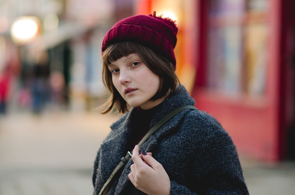 Femme en manteau gris se tient près d’un bâtiment peint en rose