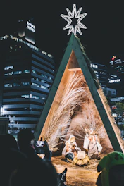Wide shot of the wooden nativity scene installed at the back of Schlossbergplatz, with the clock tower visible in the background.