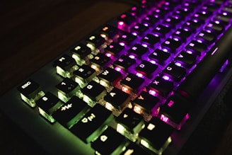 A mechanical keyboard with illuminated keys featuring a spectrum of colors including green, purple, and pink. The lighting enhances the visibility of the key symbols, giving a vibrant and tech-savvy look.