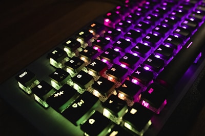 A mechanical keyboard with illuminated keys featuring a spectrum of colors including green, purple, and pink. The lighting enhances the visibility of the key symbols, giving a vibrant and tech-savvy look.
