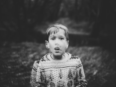 grayscale photography of boy wearing sweater frightened teams background