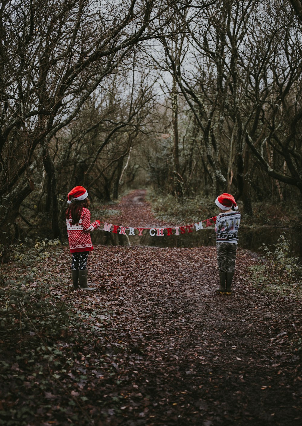 boy and girl standing on forest and holding Merry Christmas buntings