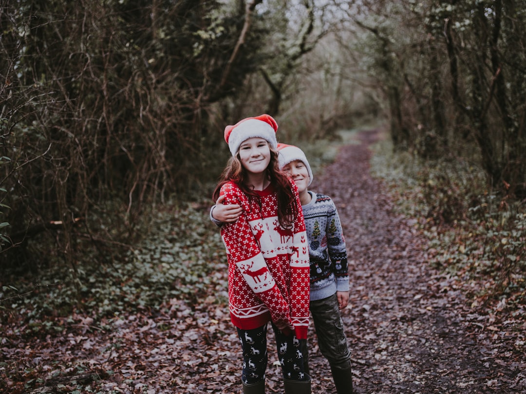 girl and boy standing between green leaf trees