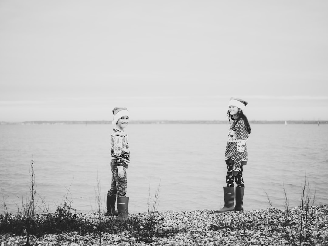 grayscale photography of boy and girl standing near body of water