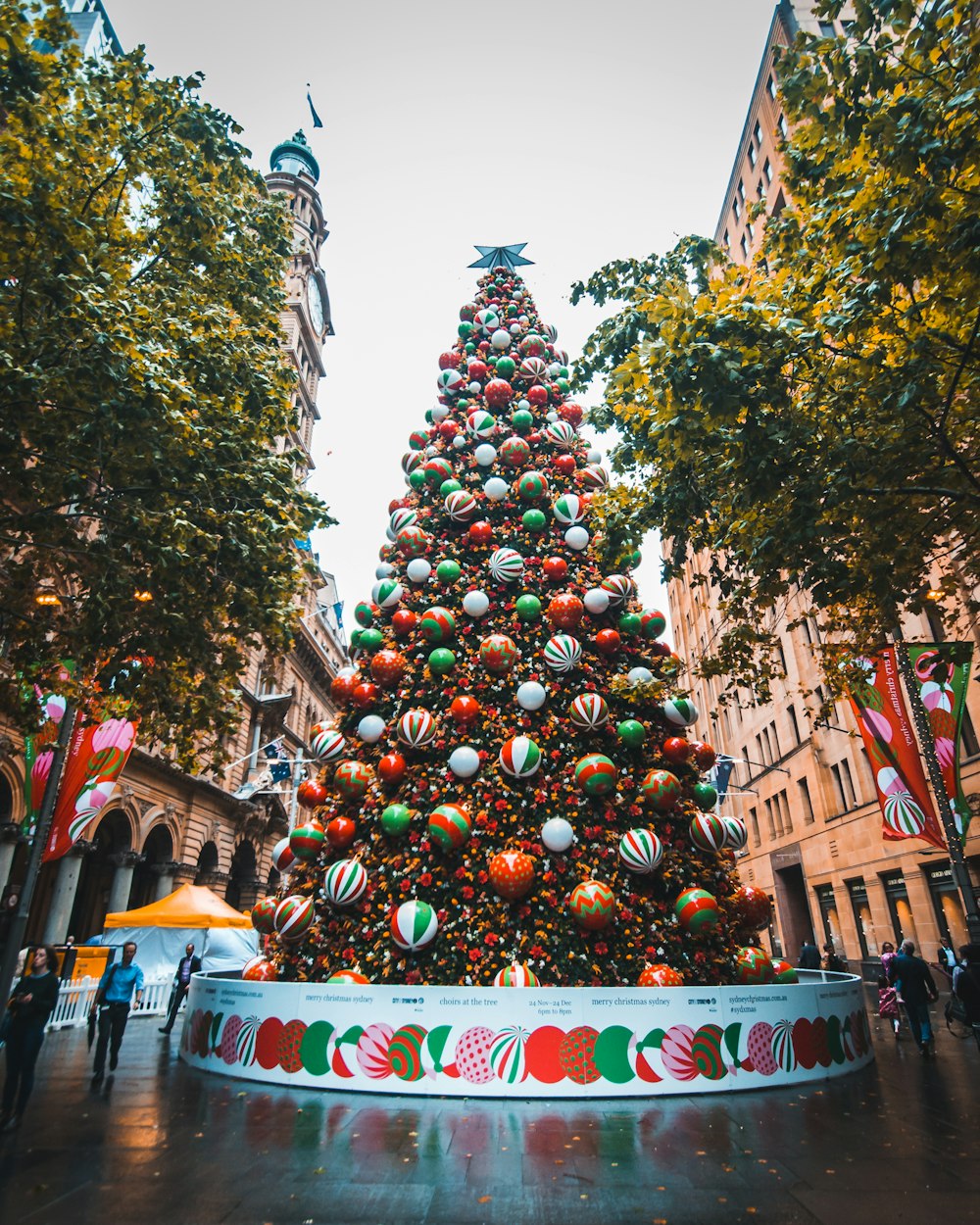 pessoas caminhando ao lado de bolas de Natal em árvore grande