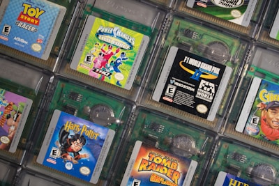 A collection of Game Boy Color cartridges is arranged in an overlapping pattern. The cartridges feature popular titles like Toy Story Racer, Power Rangers Time Force, F1 World Grand Prix, and Harry Potter. Each cartridge showcases its distinct cover art, emphasizing the diversity of games from different genres, including racing, adventure, and fantasy.