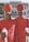 Two men are dressed in traditional red attire with matching turbans, holding silver-topped staffs. They stand in front of an ornate building with arched windows and a decorative facade. A group of people is visible in the background near the entrance. Trees flank the building, adding greenery to the scene.