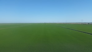 A wide aerial view of a green open plot with clear boundary markings under a bright blue sky.