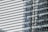 A modern building facade composed of reflective glass panels, capturing distorted images of neighboring structures. The focus is on the intricate grid pattern formed by the horizontal and vertical lines, highlighting the sleek and contemporary architectural design.