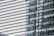 A modern building facade composed of reflective glass panels, capturing distorted images of neighboring structures. The focus is on the intricate grid pattern formed by the horizontal and vertical lines, highlighting the sleek and contemporary architectural design.