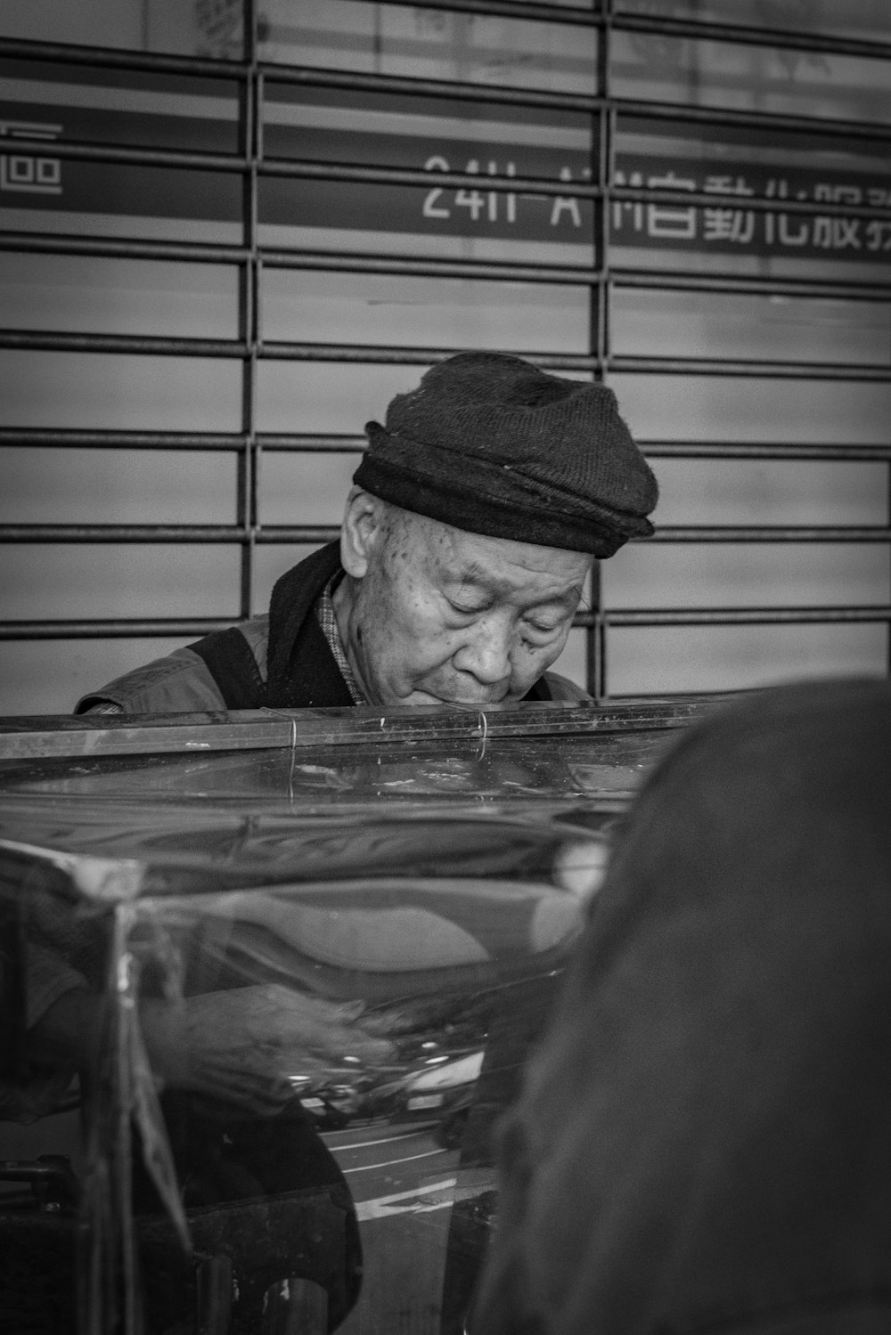 Photographie en niveaux de gris d’un homme assis à côté d’un mur