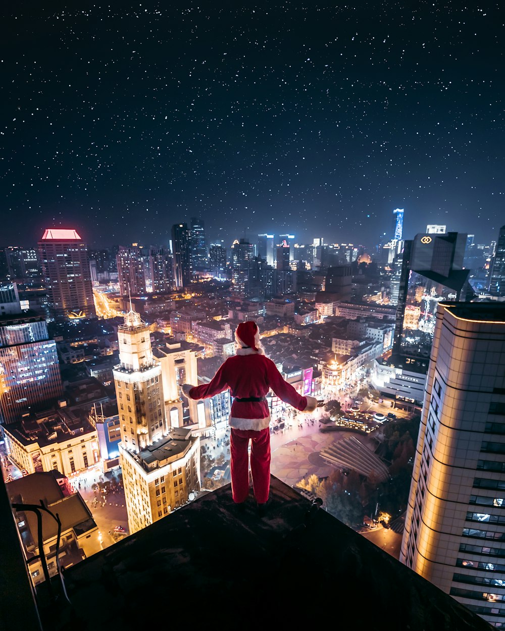 산타 클로스 복장을 입은 사람이 밤에 건물 가장자리에 서 있습니다.
