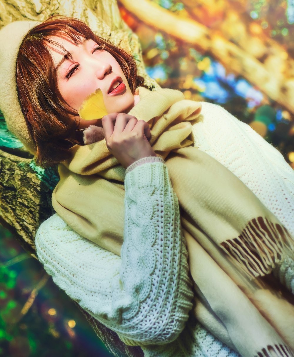woman in white knit sweater holding yellow flower