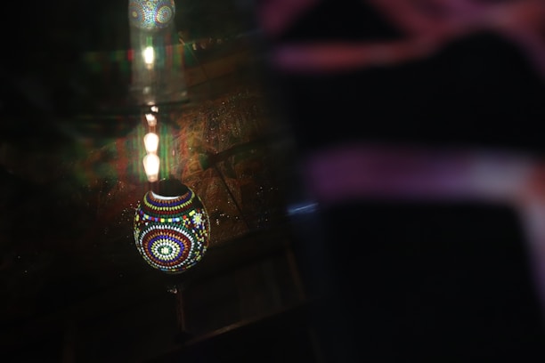 Close-up of a handcrafted wooden mosaic lamp glowing softly in a dark room.