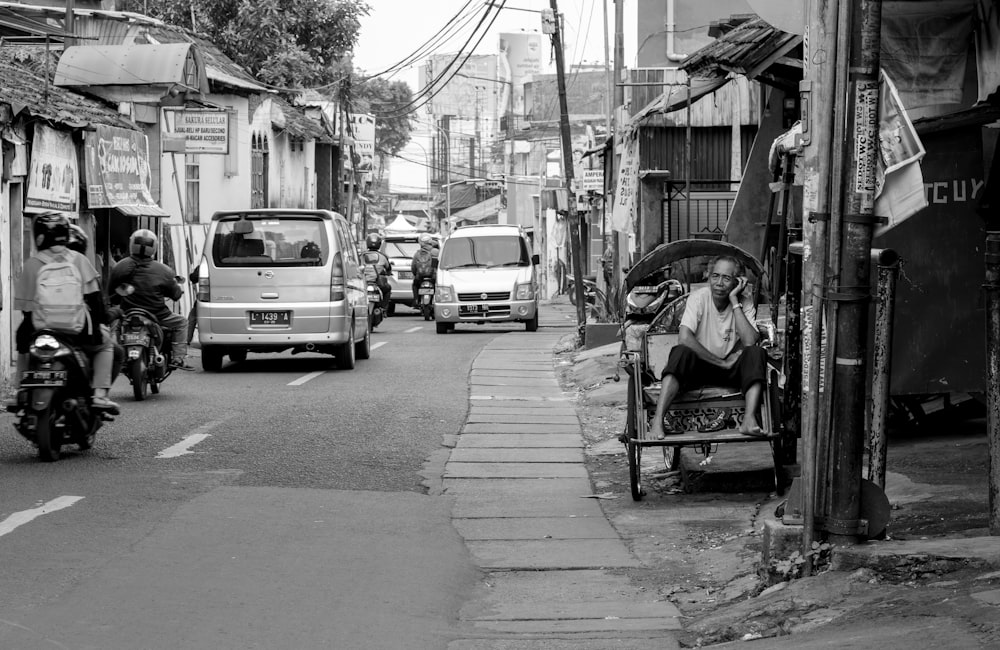 grayscale photography of man sitting on chair near road