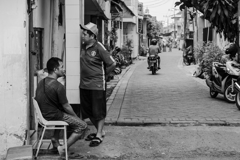 grayscale photography of man sitting on chair beside standing man