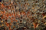 An intricate array of metal cookie cutters is organized against a pegboard with red-orange backlighting. The cutters are various shapes including animals, stars, trees, and other festive designs.