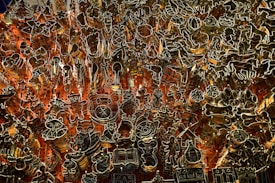 An intricate array of metal cookie cutters is organized against a pegboard with red-orange backlighting. The cutters are various shapes including animals, stars, trees, and other festive designs.