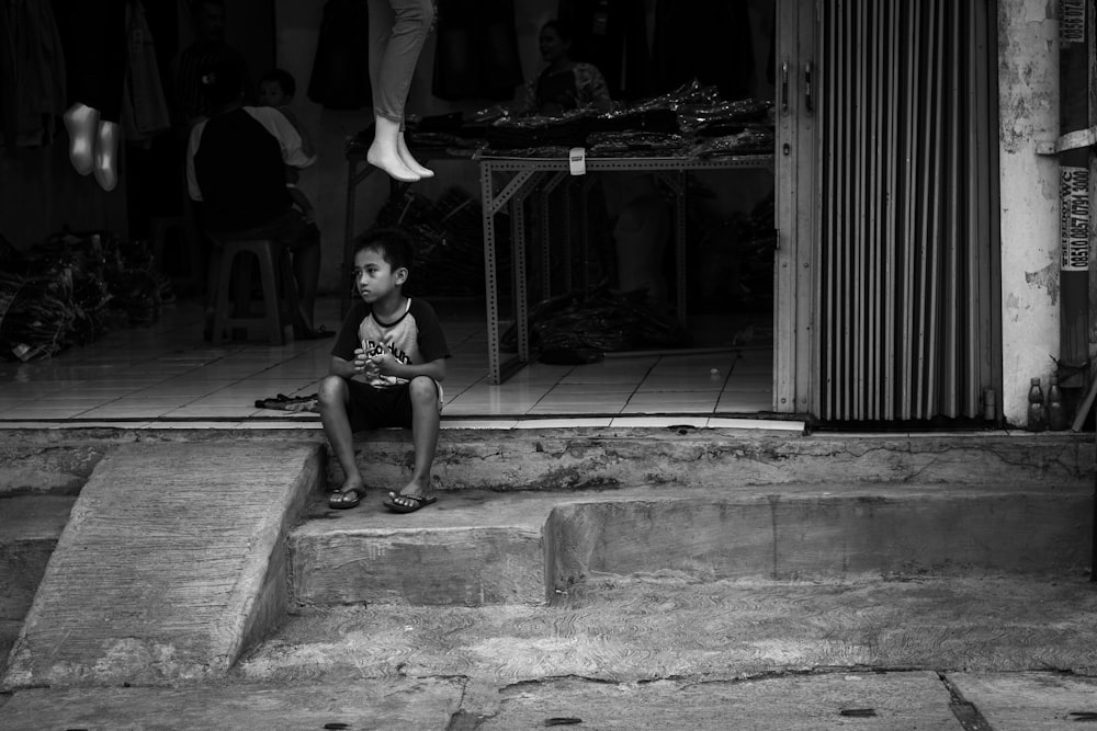 grayscale photography of boy sitting on stairs