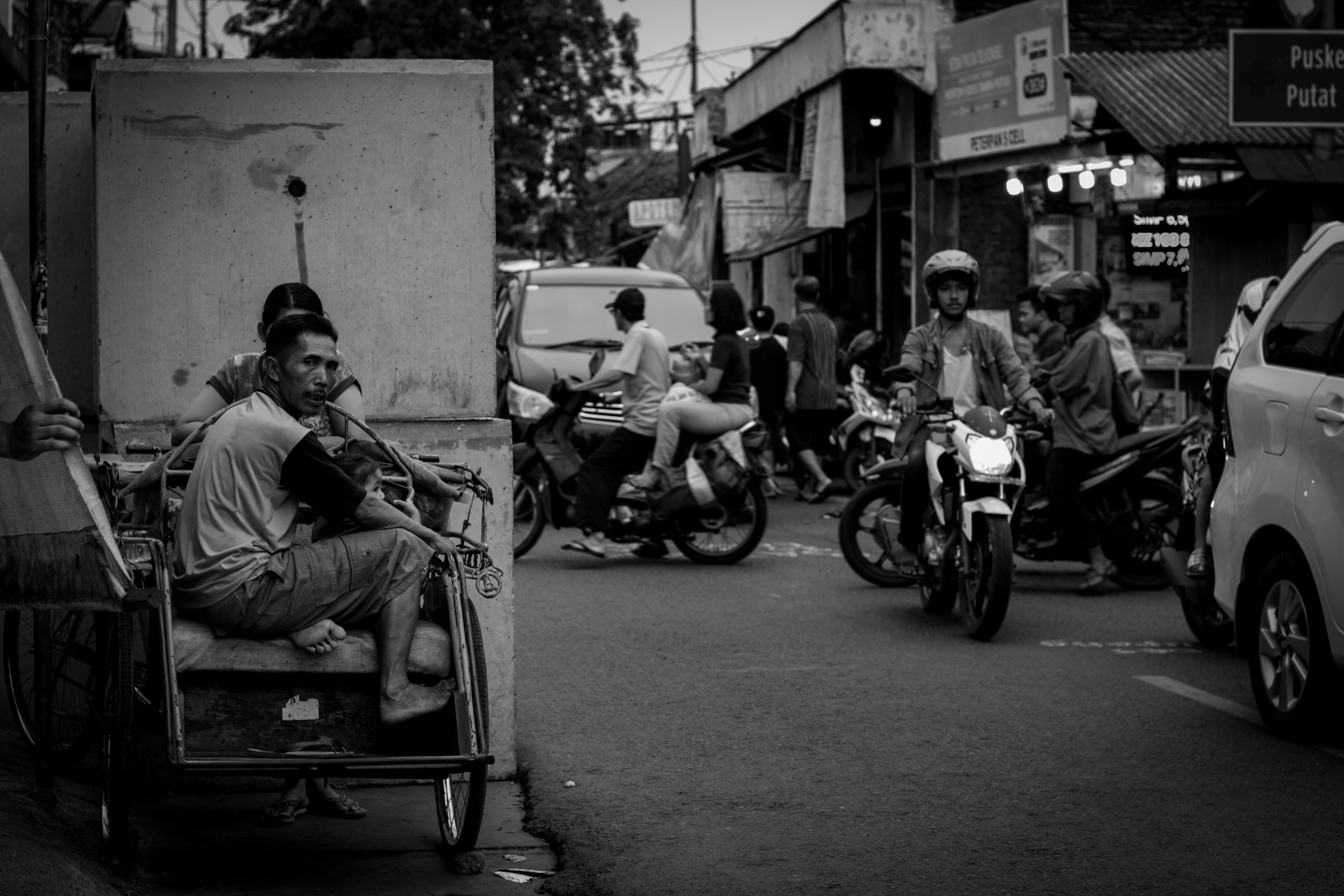Fotografi skala abu-abu pria duduk di atas roda tiga